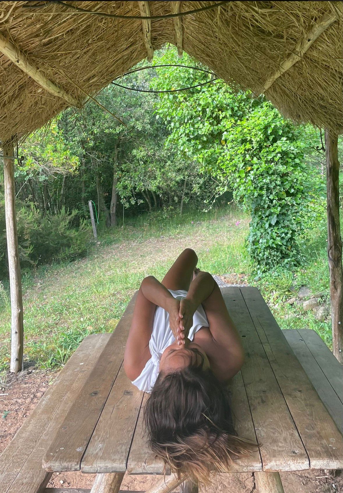 Donna distesa su tavolo di legno sotto una capanna di paglia, immersa nel verde della natura