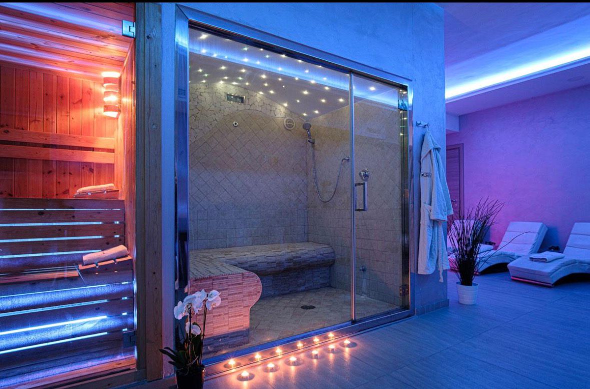 Spa wellness con cabina criosauna e bagno turco illuminati da luci LED blu e rossa, area relax con lettini