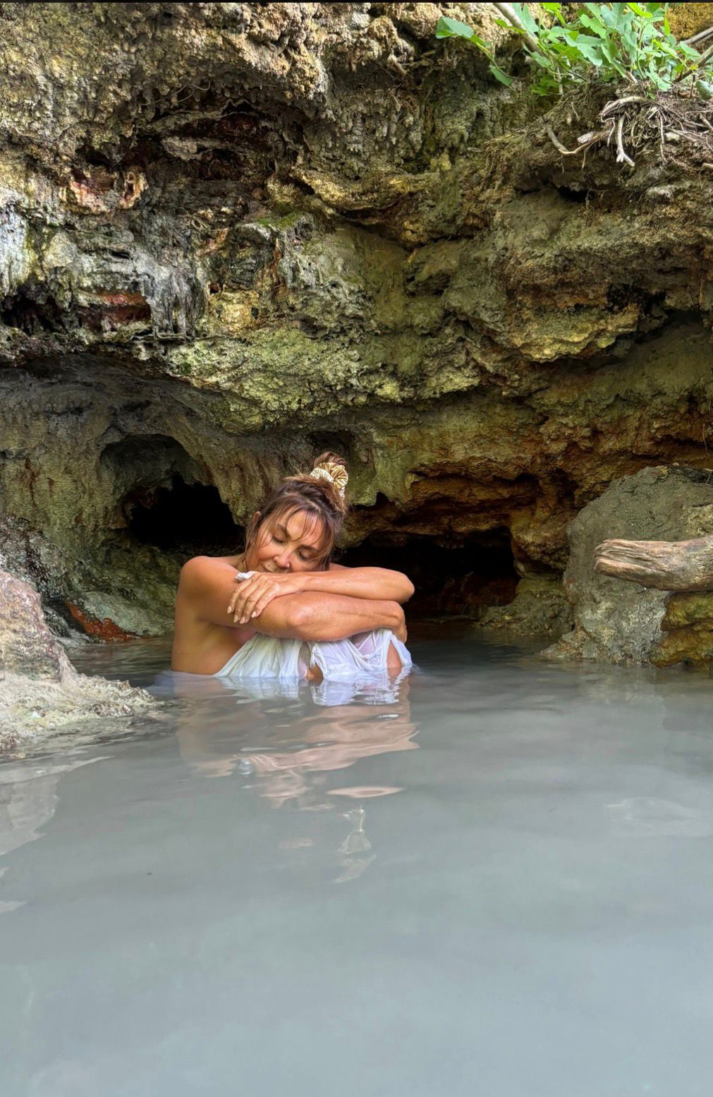 Donna rannicchiata nell'acqua bianca termale di una grotta naturale calcarea